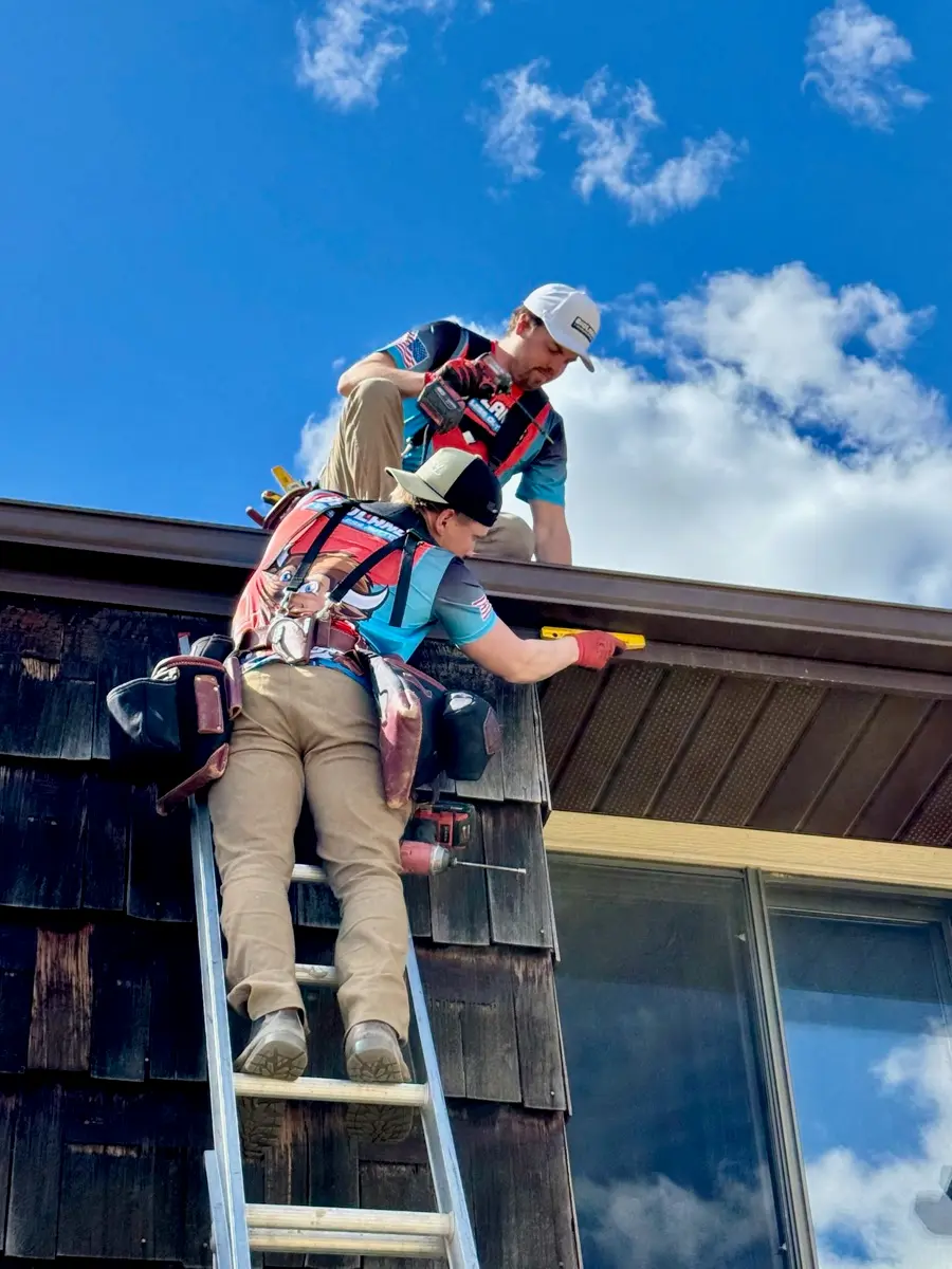 Installer fitting seamless gutter beside a window on a Delano home