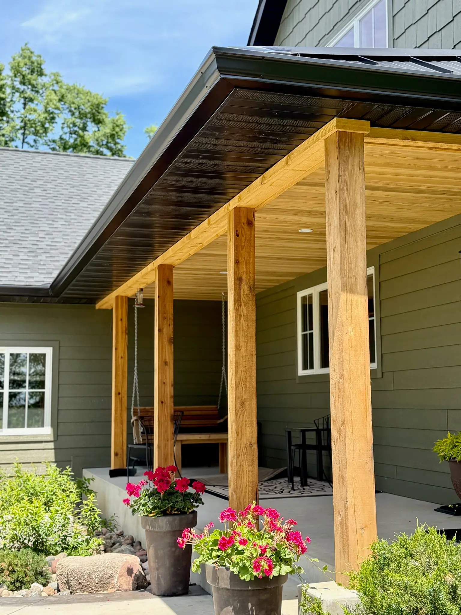 Black seamless gutters over a cedar-post porch on a green Minnesota home