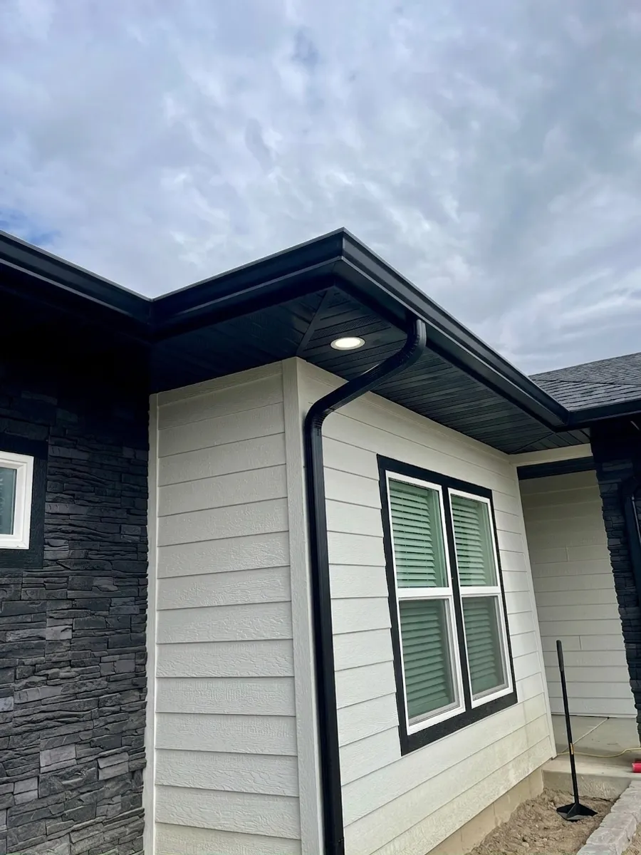 The same house with black seamless gutters and a downspout rendered on it